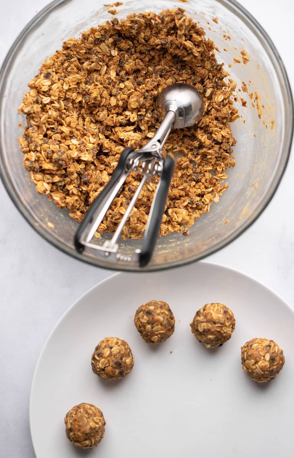A bowl of glass with a mixture of oatmeal butter next to peanut butter energy ball rolled on a white plate.